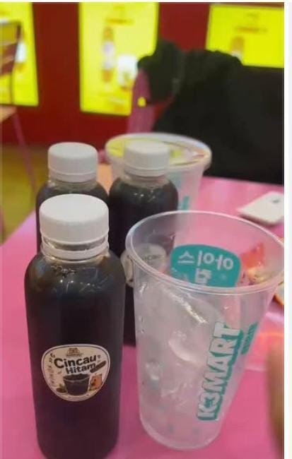 Tiga botol Es Cincau Hitam di meja bersama gelas es berlogo K3 Mart